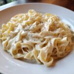 Close-up of fettuccine pasta generously coated in creamy homemade alfredo sauce and topped with cracked black pepper.