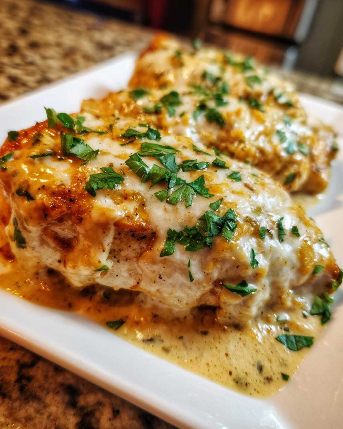 Two juicy chicken breasts covered in a creamy sauce, melted white cheese, and fresh parsley, representing fiesta lime chicken.