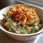 A close-up serving of creamy green bean casserole topped generously with crispy fried onions.