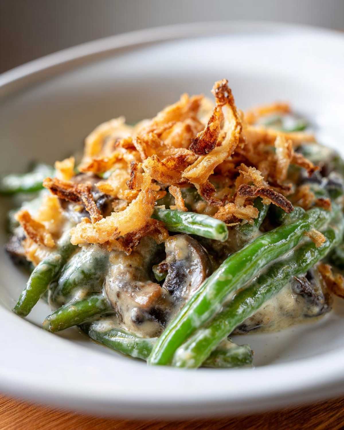 A close-up serving of creamy green bean casserole featuring bright green beans, mushrooms, and topped with crispy fried onions.