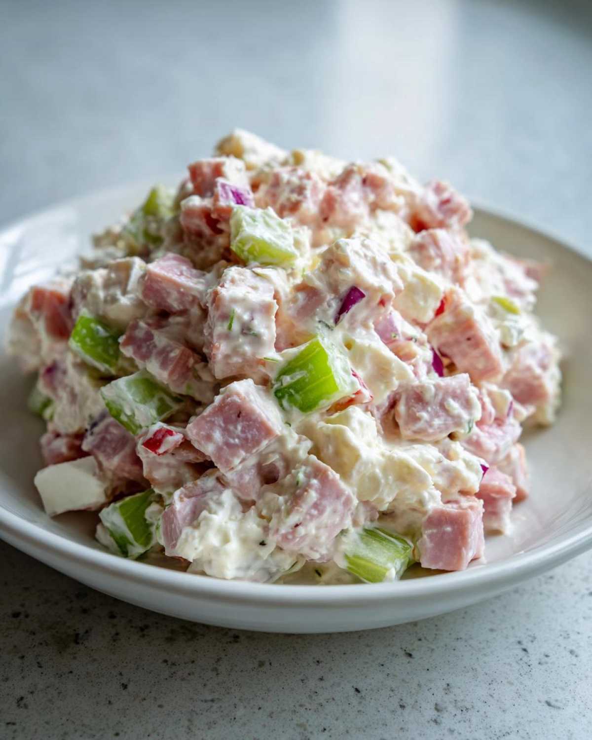 A close-up shot of creamy ham salad featuring diced pink ham, bright green celery, and purple onion mixed in a mayonnaise dressing.