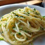 Close-up of spaghetti coated in a rich sauce, featuring bright specks of lemon zest and fresh parsley, our Creamy Lemon Pasta.