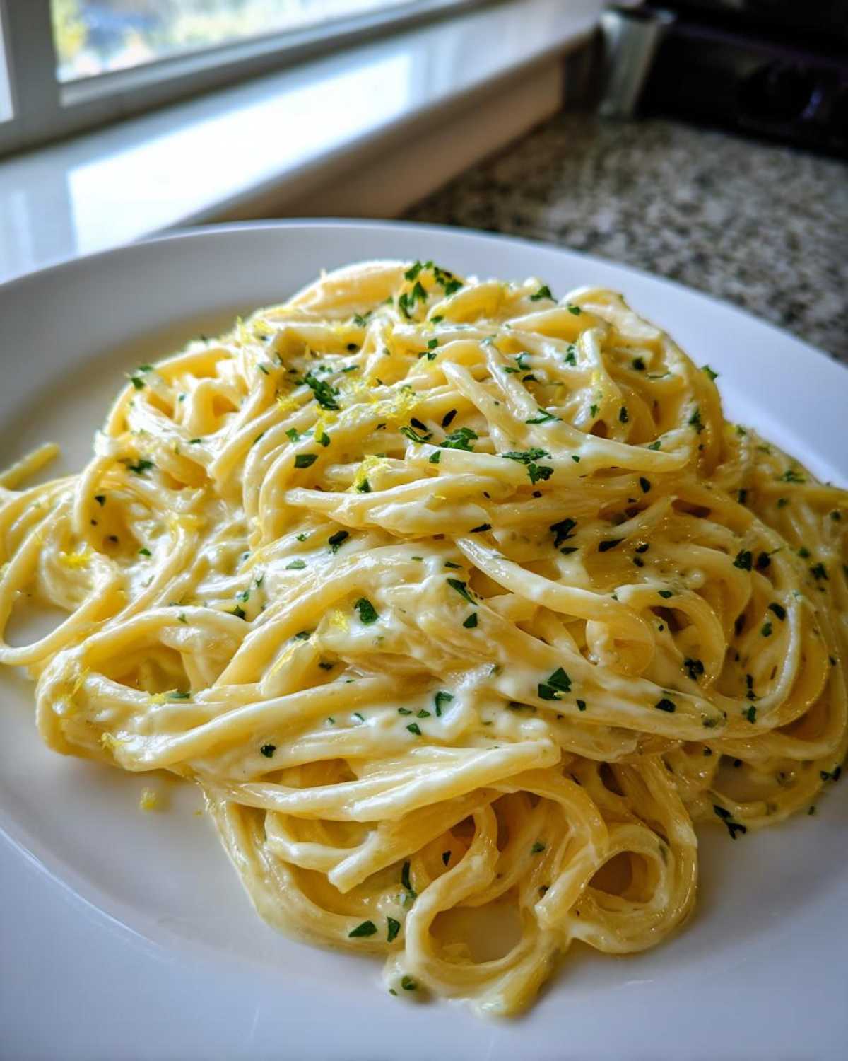 A close-up shot of a serving of rich Creamy Lemon Pasta coated in a white sauce, garnished with parsley and lemon zest.