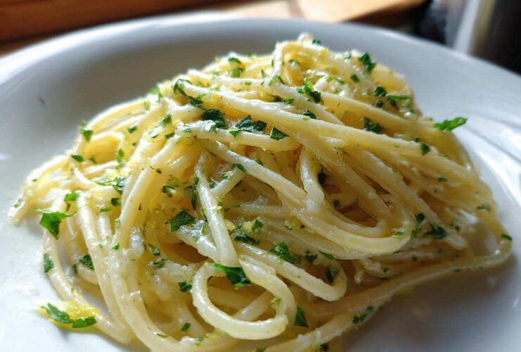 Close-up of spaghetti coated in a rich sauce, featuring bright specks of lemon zest and fresh parsley, our Creamy Lemon Pasta.