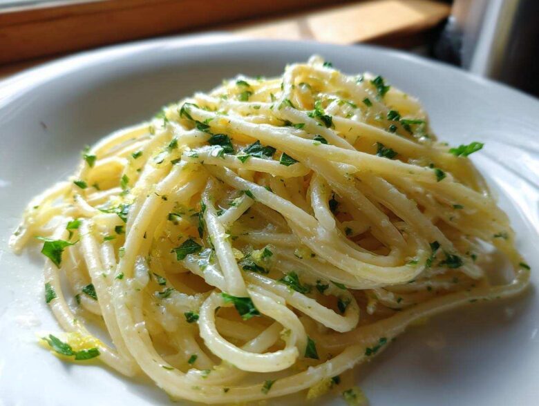 Close-up of spaghetti coated in a rich sauce, featuring bright specks of lemon zest and fresh parsley, our Creamy Lemon Pasta.