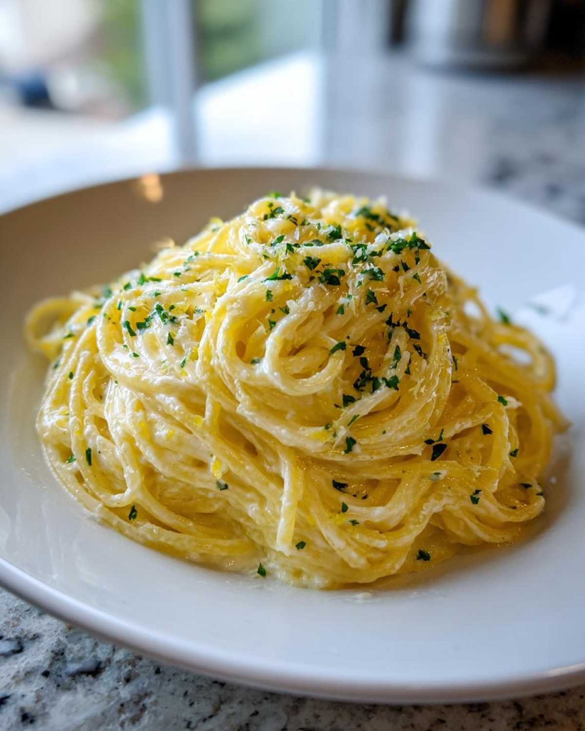 A close-up of a generous serving of Creamy Lemon Pasta, topped with grated cheese and fresh chopped parsley.