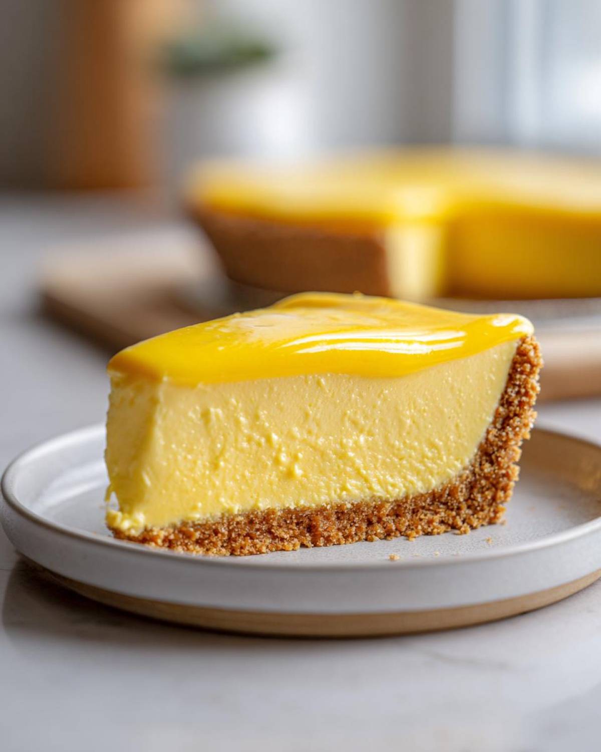A close-up of a thick slice of creamy lemon pie with a graham cracker crust and glossy yellow topping.
