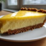 Close-up of a thick slice of creamy lemon pie with a graham cracker crust on a white plate.