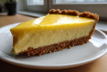 Close-up of a thick slice of creamy lemon pie with a graham cracker crust on a white plate.