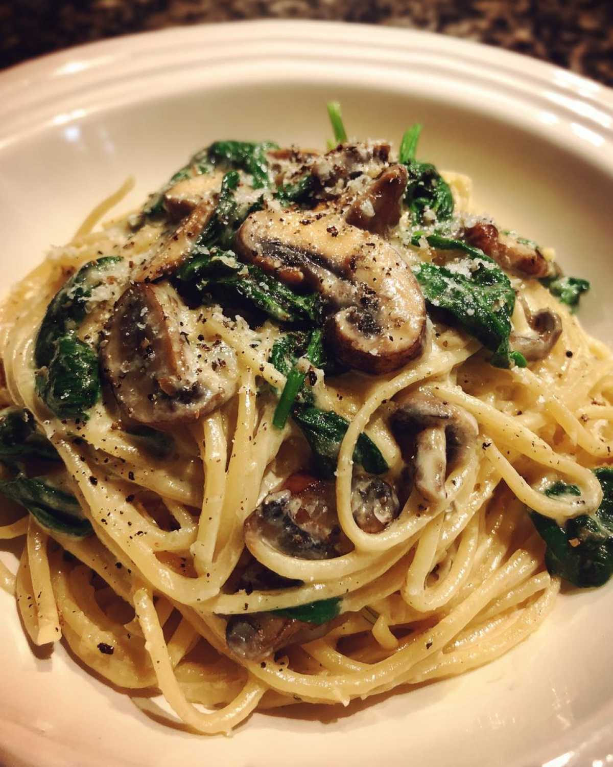 A close-up of creamy mushroom pasta featuring sautéed mushrooms and wilted spinach, topped with grated cheese and black pepper.