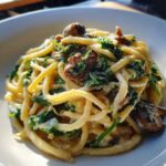 Close-up of creamy mushroom pasta mixed with wilted spinach served in a white bowl.