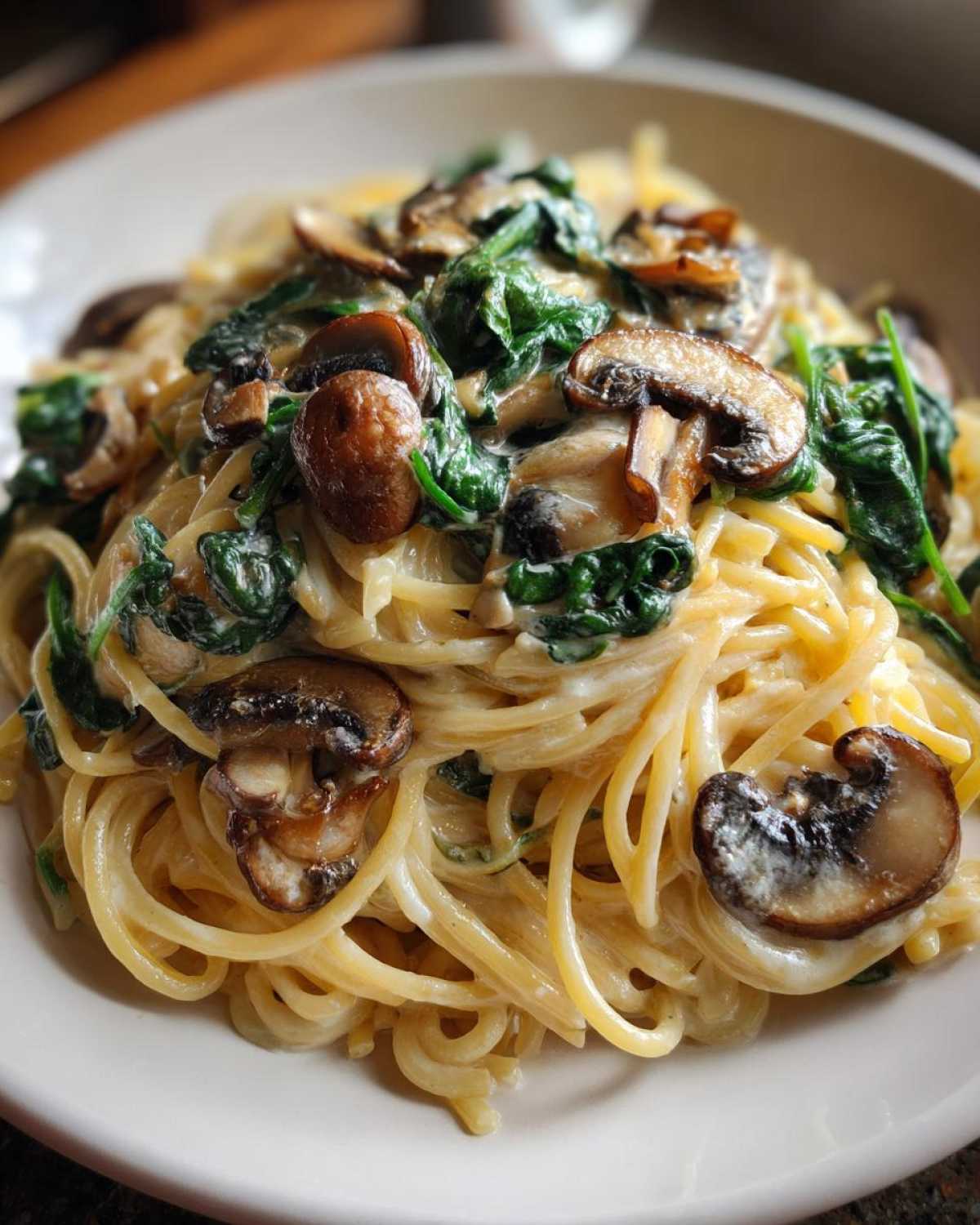Close-up of creamy mushroom pasta tossed with wilted spinach, served on a white plate.