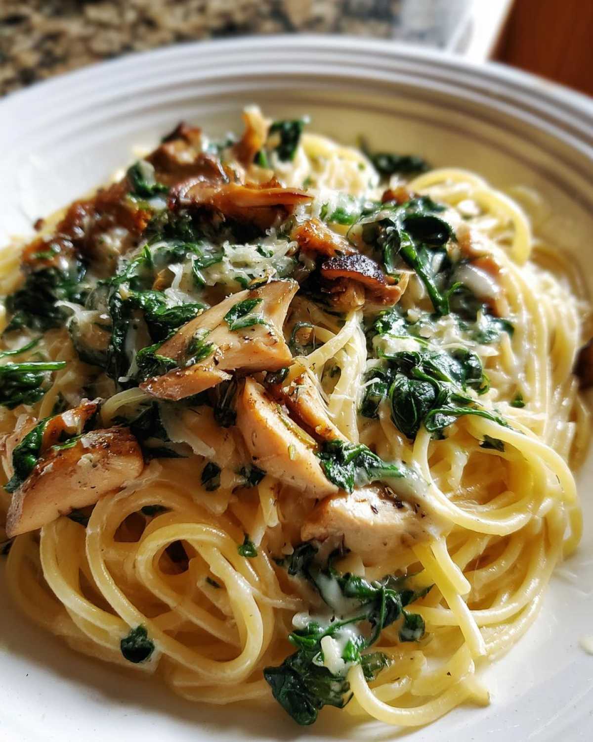 Close-up of creamy mushroom pasta featuring spaghetti, sautéed mushrooms, spinach, and grated Parmesan cheese.