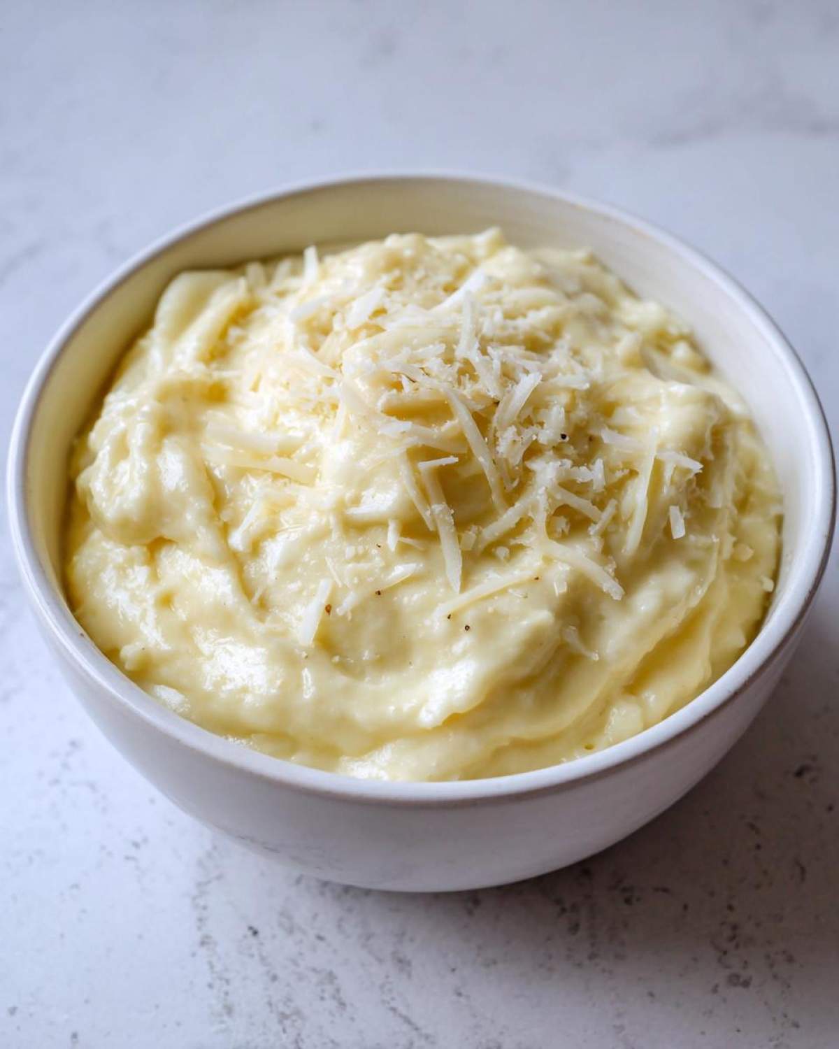 A close-up of creamy, rich Olive Garden Alfredo Sauce topped with freshly grated Parmesan cheese in a white bowl.