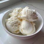 Four generous scoops of creamy, white protein ice cream served in a small white bowl.
