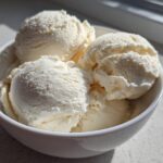 Four generous scoops of creamy vanilla-colored protein ice cream served in a small white bowl.
