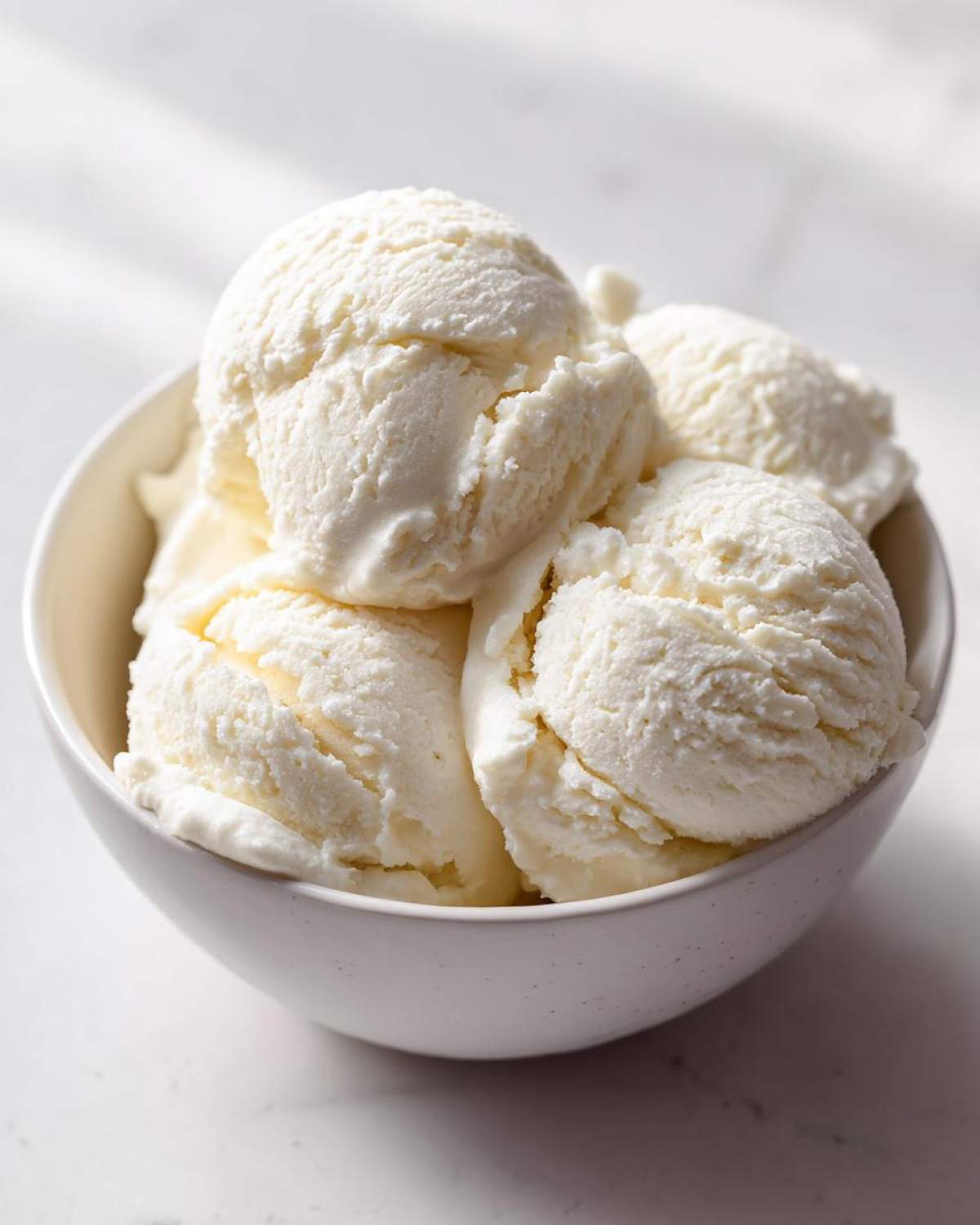 Close-up of several scoops of light-colored, creamy protein ice cream served in a white bowl.