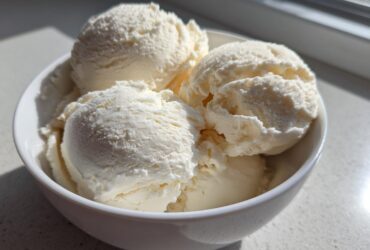Four generous scoops of creamy vanilla-colored protein ice cream served in a small white bowl.