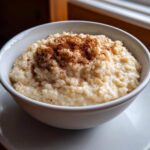 A close-up of creamy rice pudding topped generously with ground cinnamon in a white bowl.