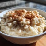 A close-up of creamy rice pudding in a white bowl, generously sprinkled with ground cinnamon.