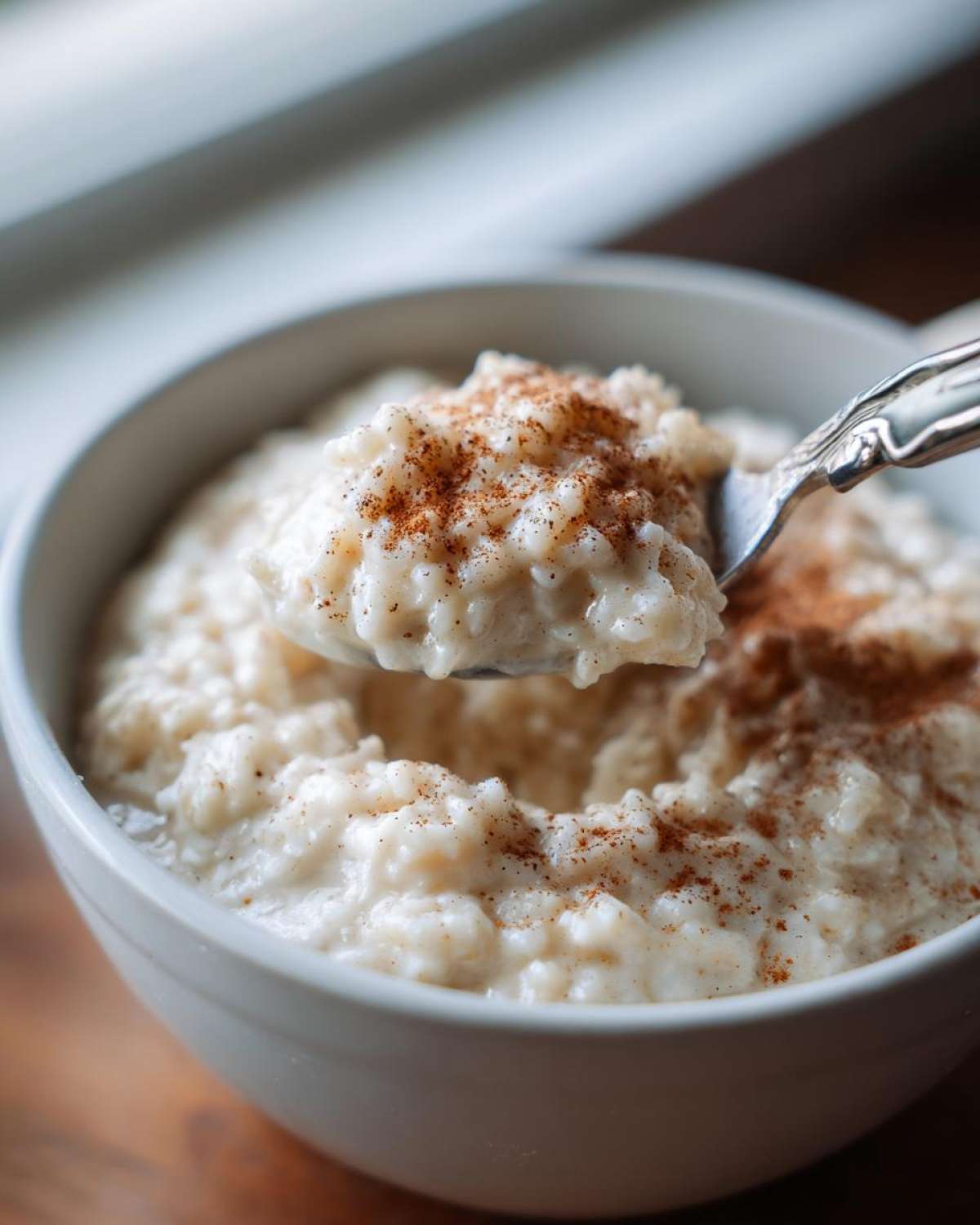 A spoonful of creamy rice pudding topped with cinnamon being lifted from a white bowl.