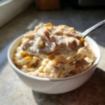 A spoonful of creamy crockpot white chicken chili, featuring shredded chicken and white beans, lifted from a white bowl.