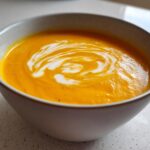 Close-up of a bowl of bright orange squash soup topped with a swirl of cream.