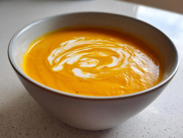 Close-up of a bowl of bright orange squash soup topped with a swirl of cream.