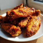 A pile of golden brown, crispy baked chicken wings seasoned with spices, served on a white plate.