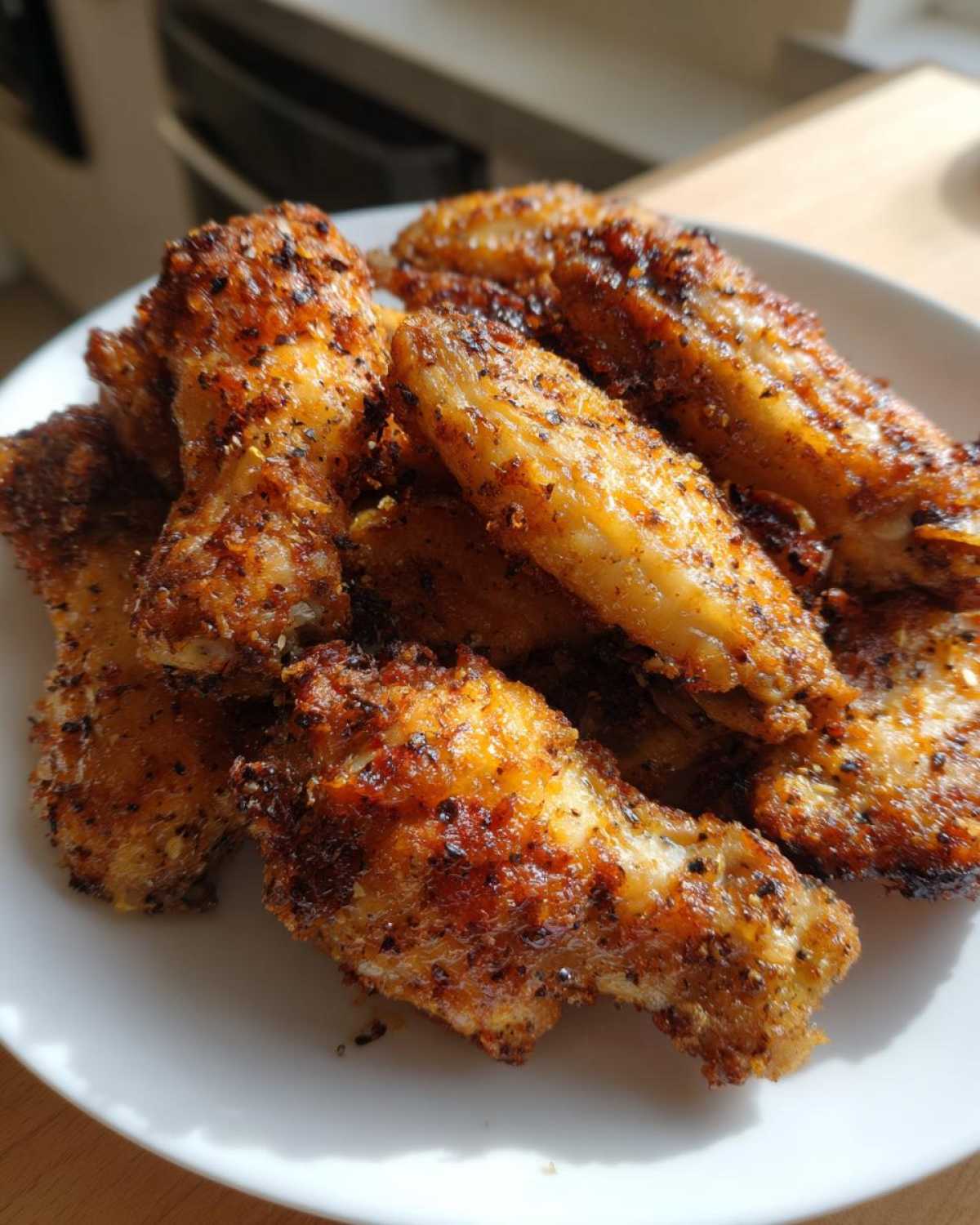 Close-up of golden brown, seasoned crispy baked chicken wings piled high on a white plate.