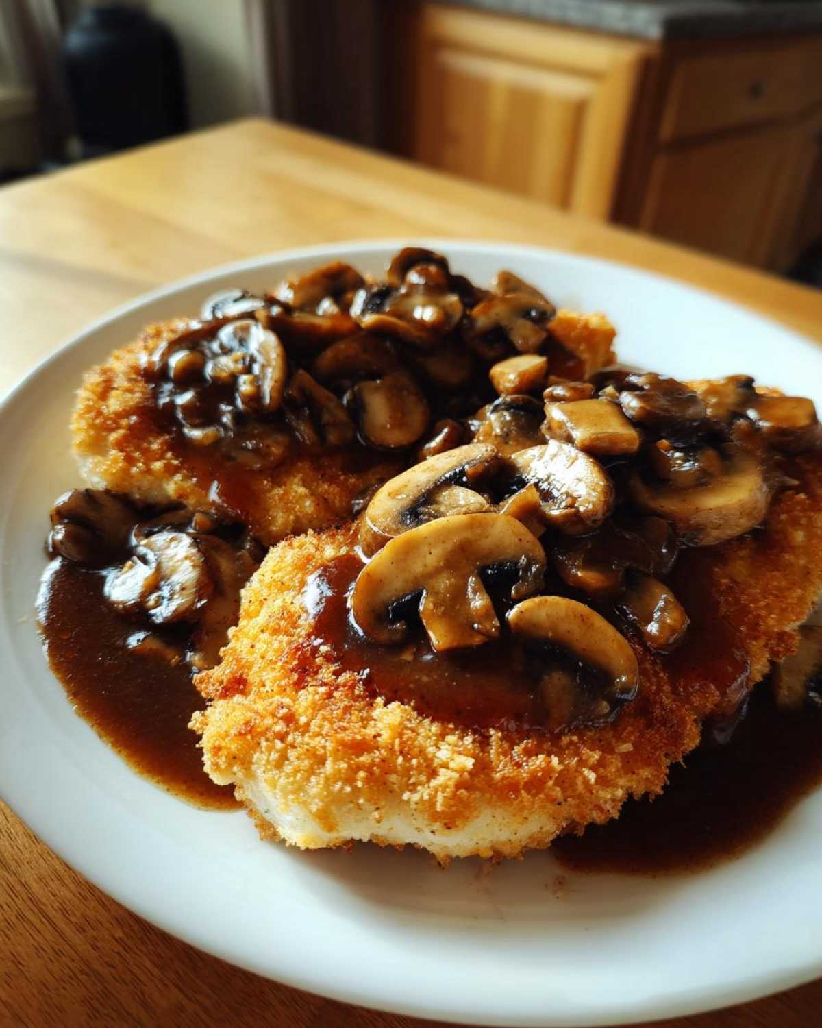 Two breaded cutlets of Chicken Marsala topped generously with sliced mushrooms in a dark brown sauce.