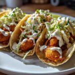 Three delicious fish tacos featuring crispy fried fish, crunchy slaw, and a drizzle of white sauce on soft tortillas.
