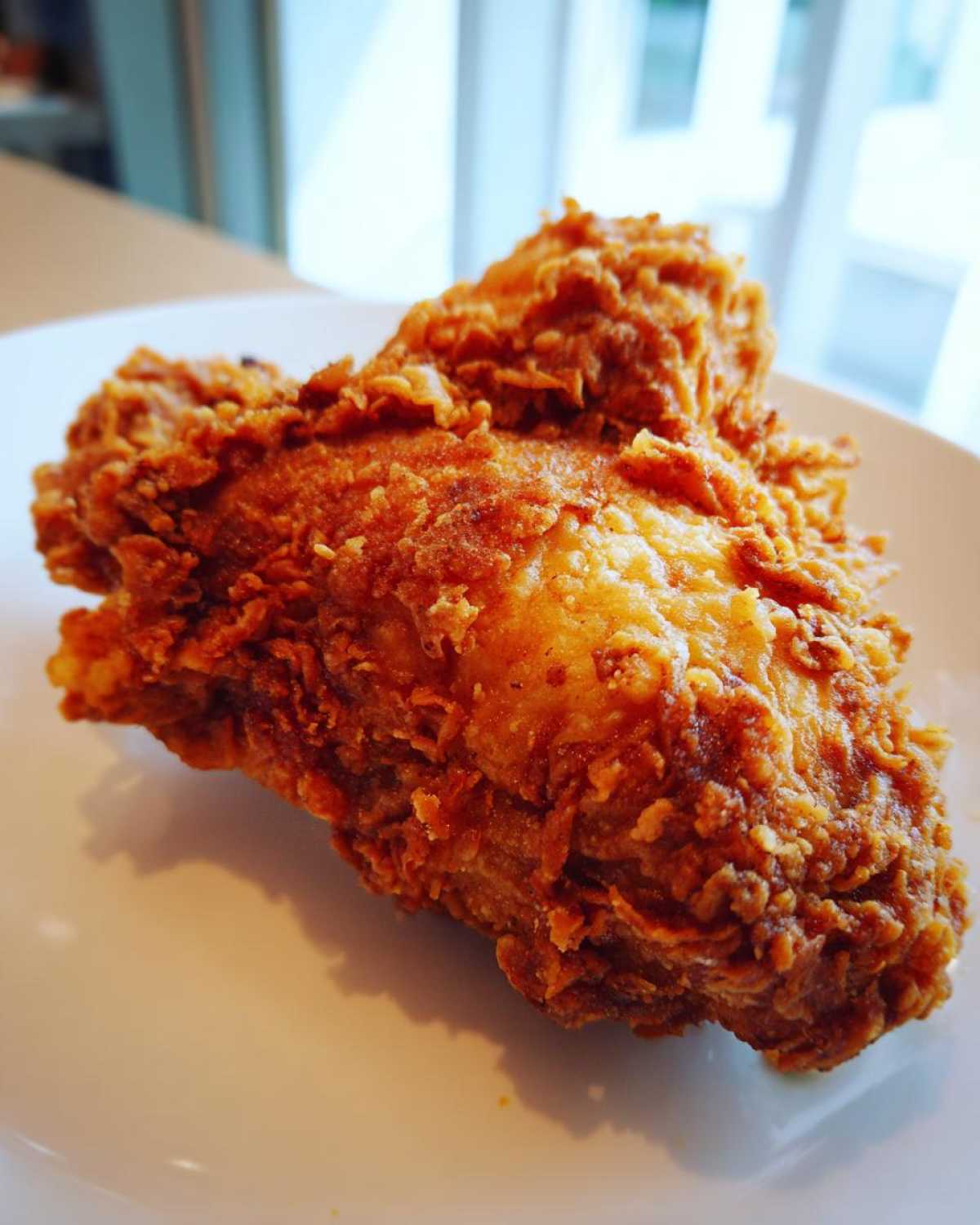 Close-up of a perfectly golden-brown, crispy piece of fried chicken resting on a white plate.