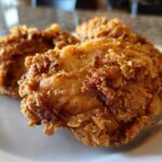 Close-up of several pieces of golden brown, crispy fried chicken resting on a white plate.