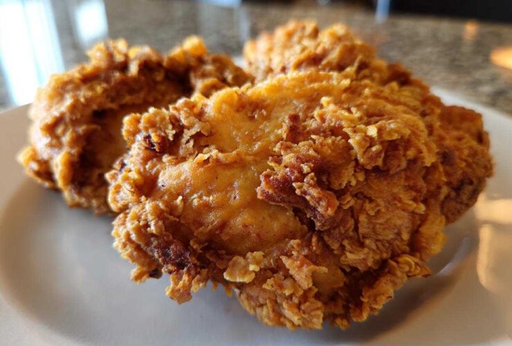Close-up of several pieces of golden brown, crispy fried chicken resting on a white plate.