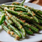 Close-up of bright green beans topped with crispy, browned breadcrumbs served on a white plate.