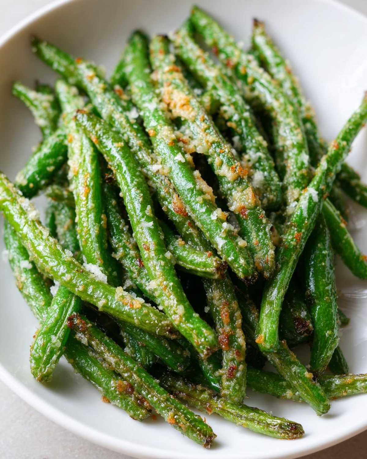 Close-up of bright green beans roasted and topped with crispy Parmesan cheese.