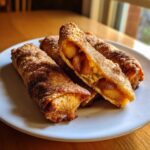 Close-up of crispy, cinnamon-sugar coated peach cobbler egg rolls, one cut open showing the warm peach filling.