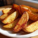 A close-up of golden brown, crispy potato wedges seasoned with spices, piled on a white plate.