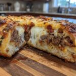 Close-up of a cross-section of baked garbage bread showing melted cheese pull and savory meat filling inside golden dough.