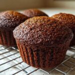 Close-up of three dark, moist bran muffins cooling on a wire rack after baking.