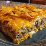 A close-up slice of Dorito Casserole showing layers of seasoned ground beef, melted cheese, and a topping of crushed chips.