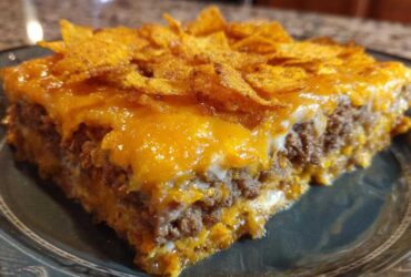 A close-up slice of Dorito Casserole showing layers of seasoned ground beef, melted cheese, and a topping of crushed chips.