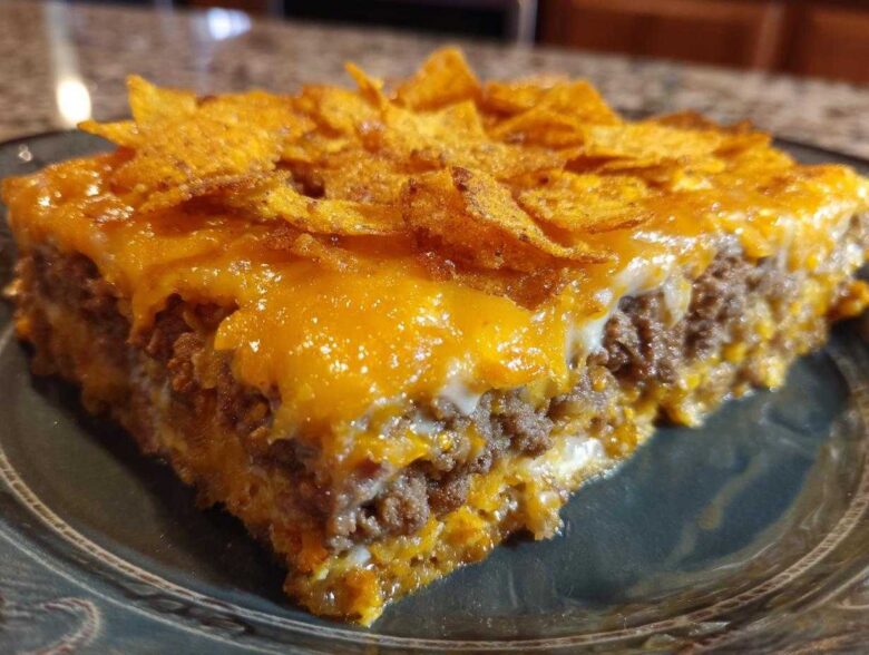A close-up slice of Dorito Casserole showing layers of seasoned ground beef, melted cheese, and a topping of crushed chips.