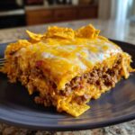A close-up serving of Dorito Casserole featuring layers of seasoned ground beef and melted cheddar cheese, topped with chips.