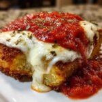 Close-up of a breaded chicken breast topped with melted mozzarella, marinara sauce, and herbs for Easy Chicken Parmesan.