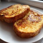 Two golden brown slices of easy french toast drizzled with syrup on a white plate.