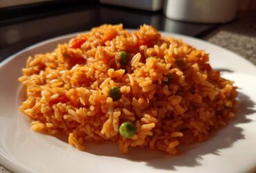 A close-up of a serving of bright orange Spanish rice with visible peas and tomato pieces on a white plate.