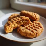 Four golden brown Easy Peanut Butter Cookies on a plate, one broken open to show the soft interior.