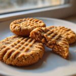 Four classic Easy Peanut Butter Cookies on a white plate, one broken open to show the texture.
